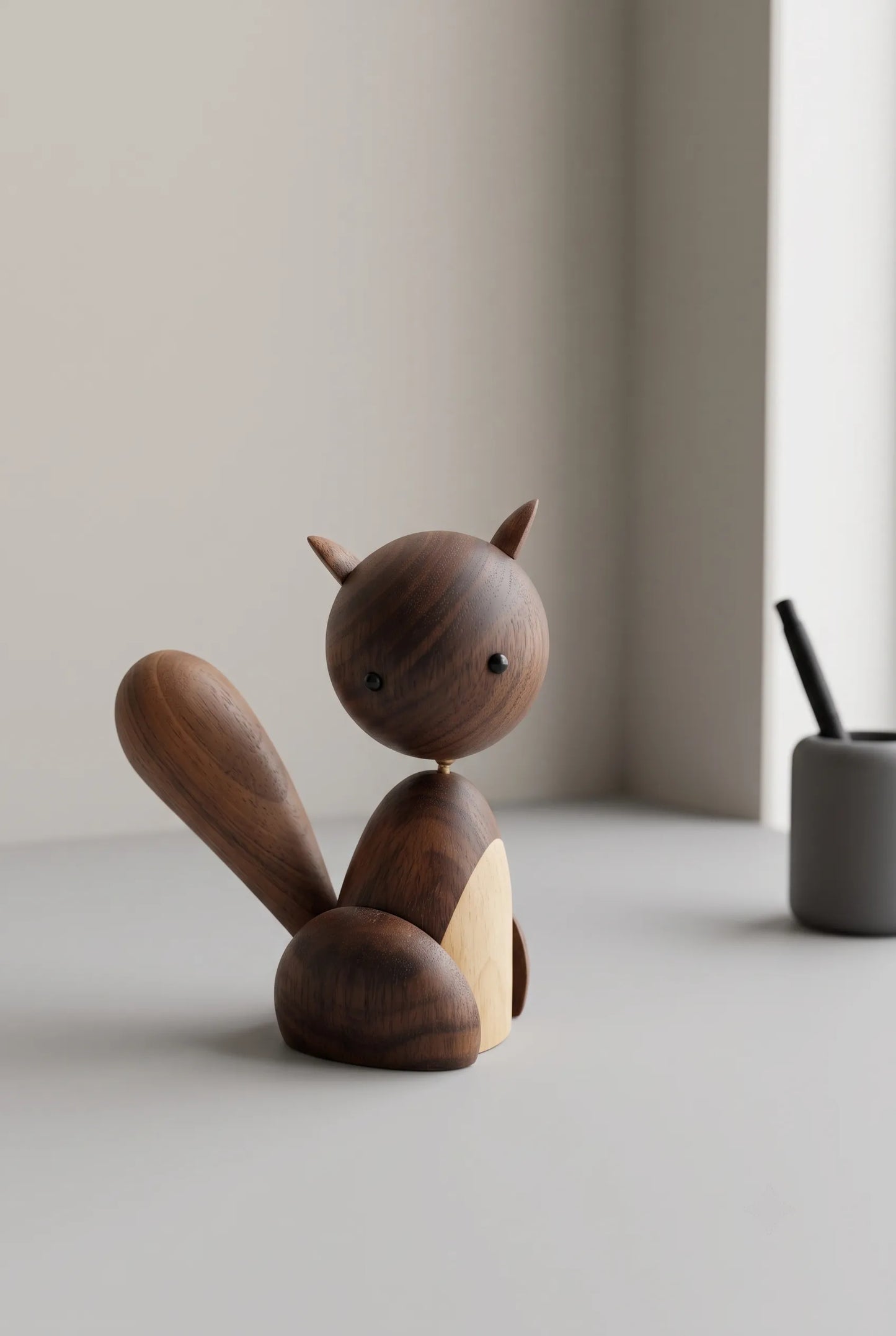 Nordic black walnut squirrel sculpture on a quiet reading-nook shelf with open space around its tail.