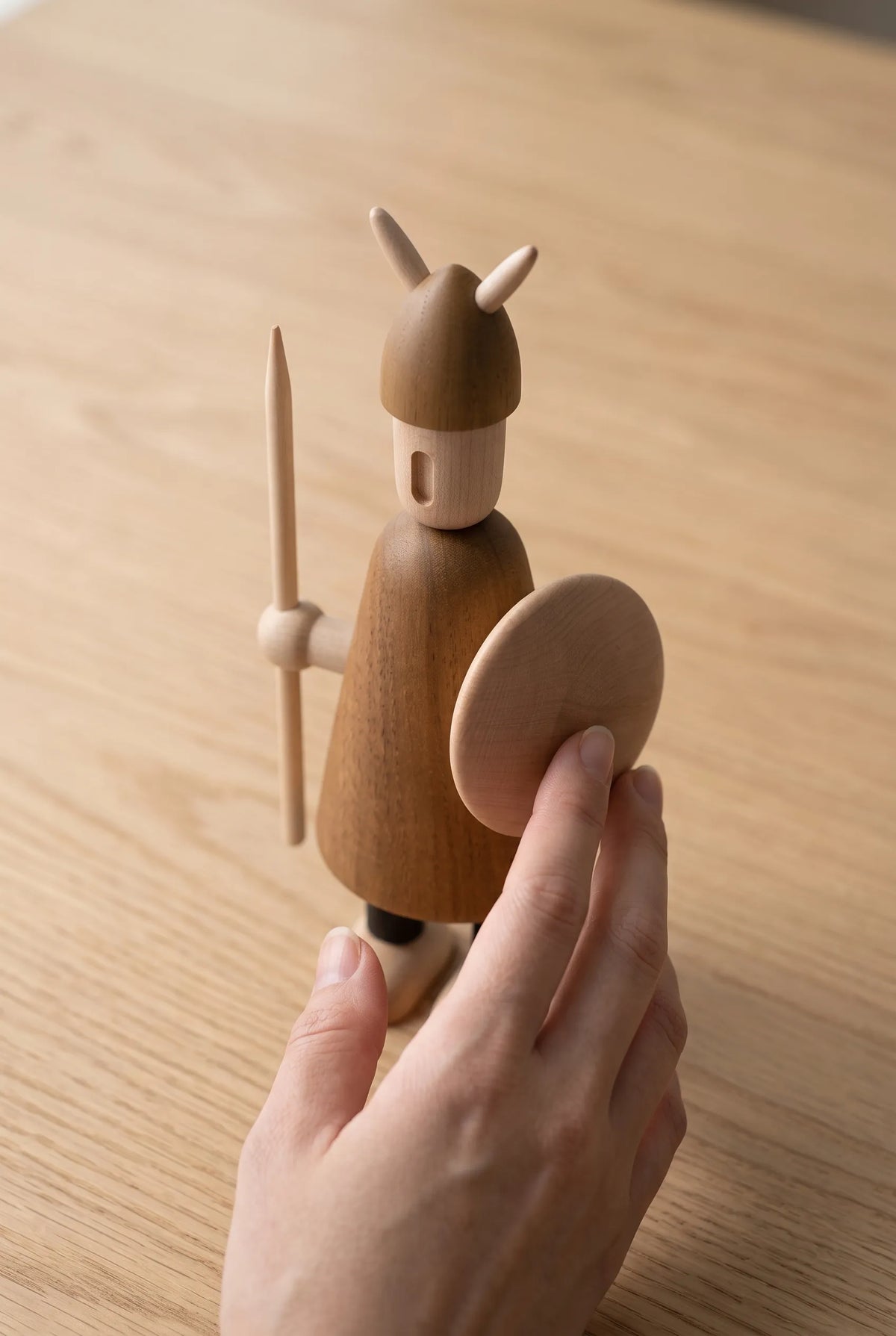 Nordic Mythos Viking Wood Sculpture crafted from Solid Teak and Natural Maple Wood with light-absorbing matte wood grain finish, touched gently by a relaxed hand at the lower frame edge.